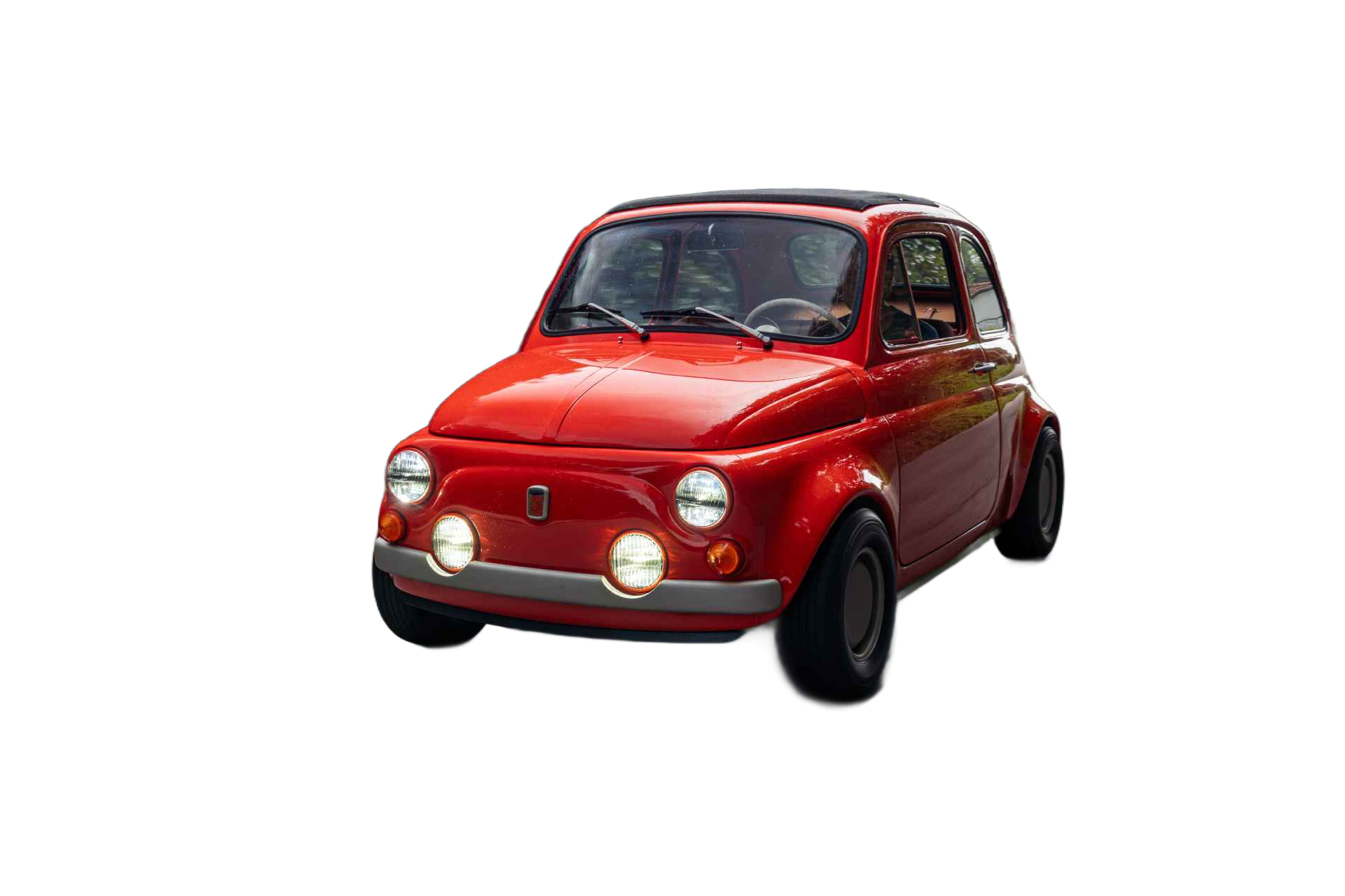 El coche cl&aacute;sico rojo, con un dise&ntilde;o retro, se desplaza por una carretera tranquila flanqueada por una densa vegetaci&oacute;n. Su estilo distintivo y faros brillantes lo hacen destacar en el entorno.